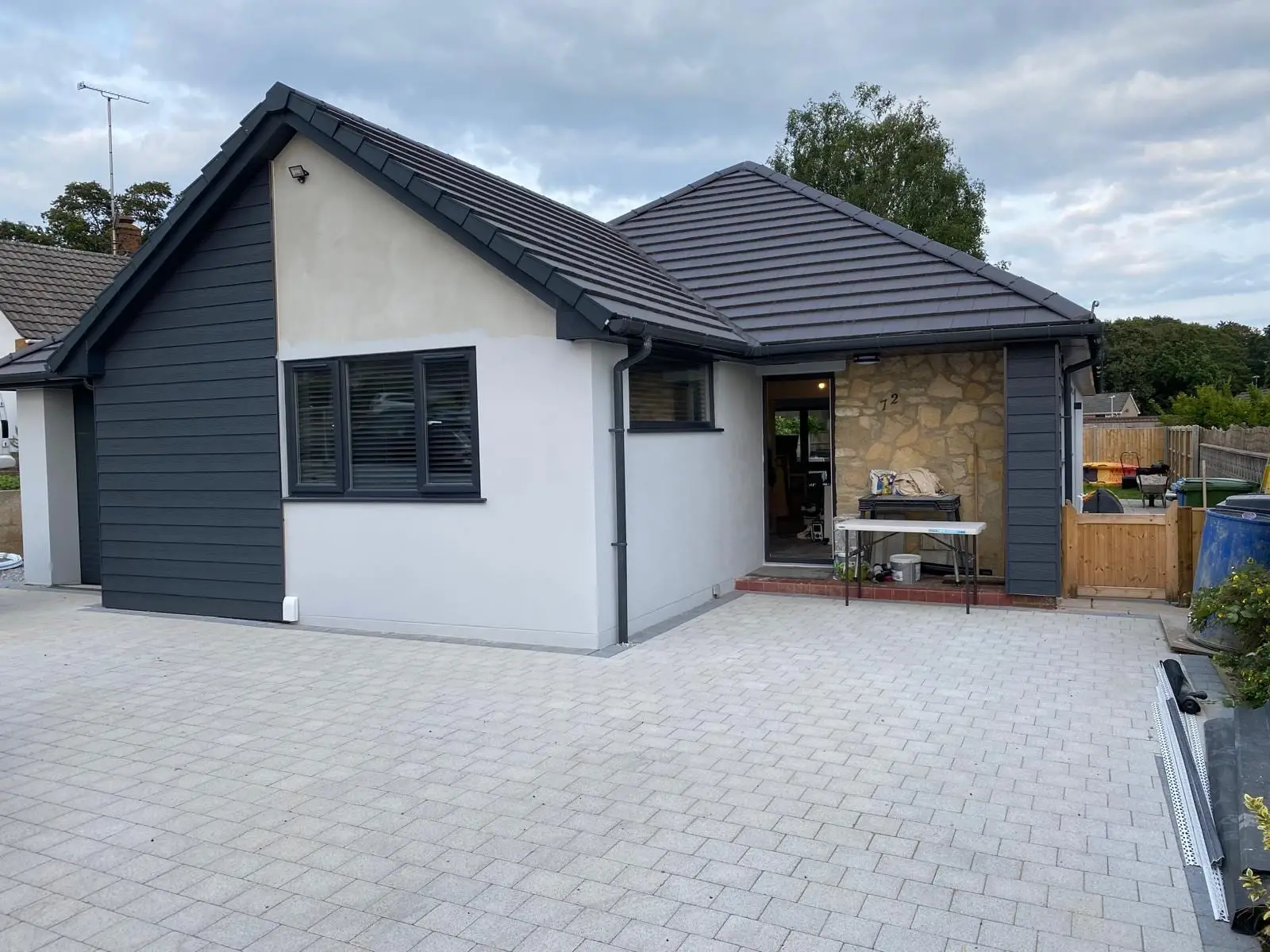 The finished bungalow in white render and dark grey cladding with a natural stone panel and a dark tiled roof