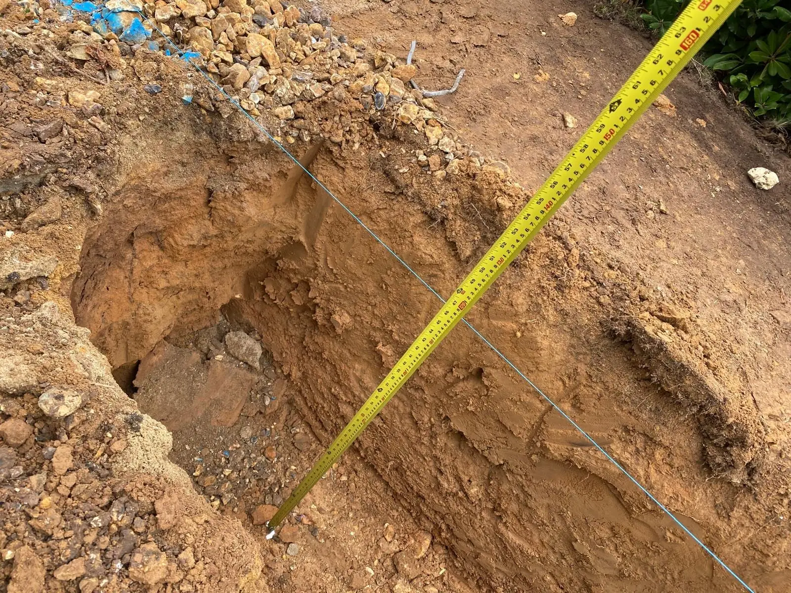 A foundation excavation with a tape measure showing the depth through sandy subsoil