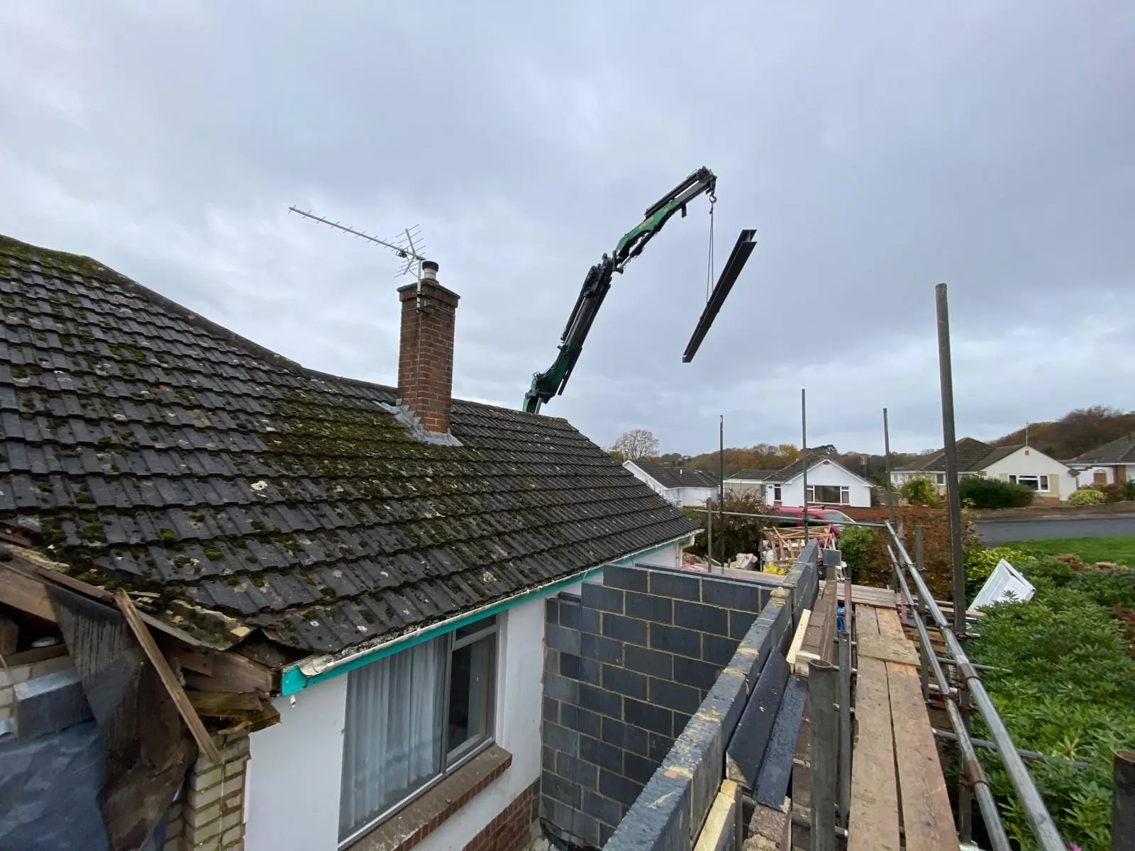 A steel beam swinging in over the bungalow roof on a lorry-mounted crane