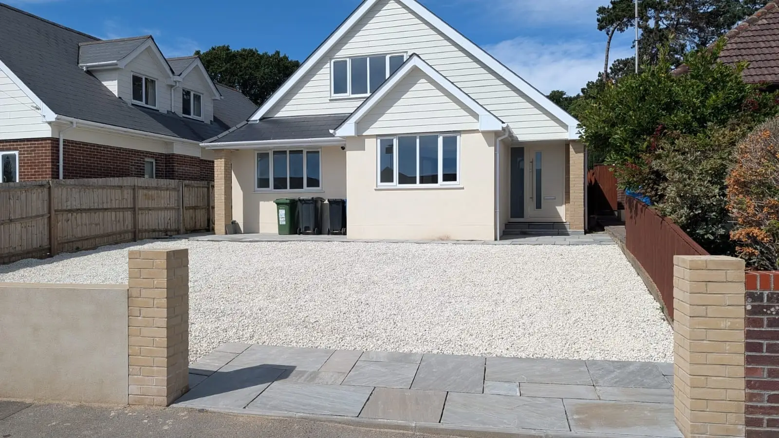 The finished chalet house in cream render and weatherboard, with a new gravel drive and sandstone paving