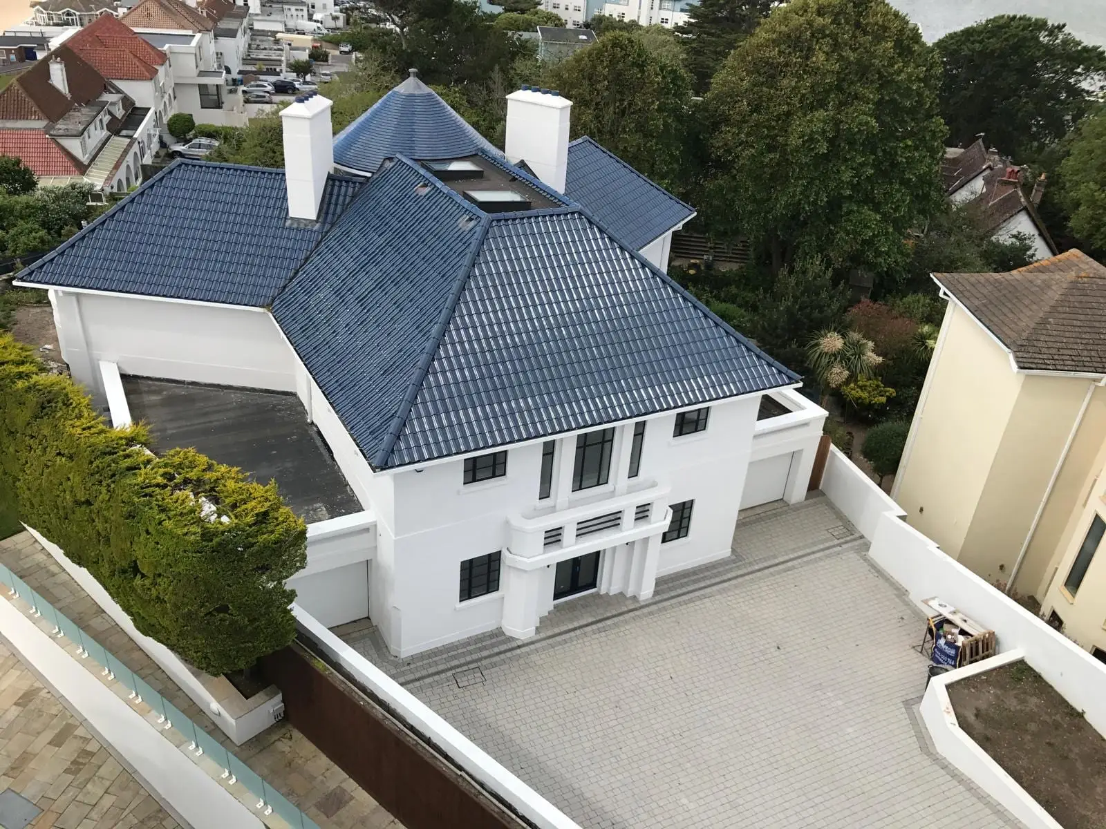 The finished house from above: white render, a blue glazed pantile roof and a block-paved forecourt