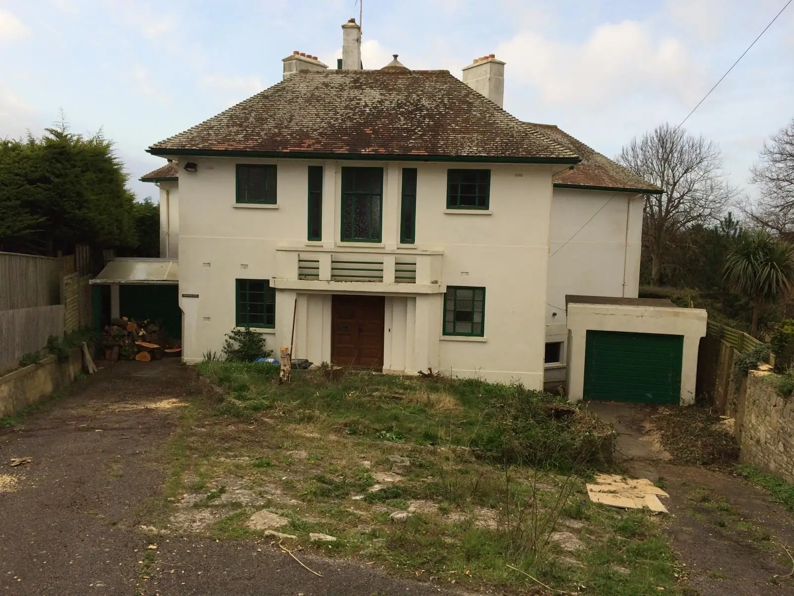 The house before work started, with a worn clay tile roof, green painted joinery and an overgrown plot