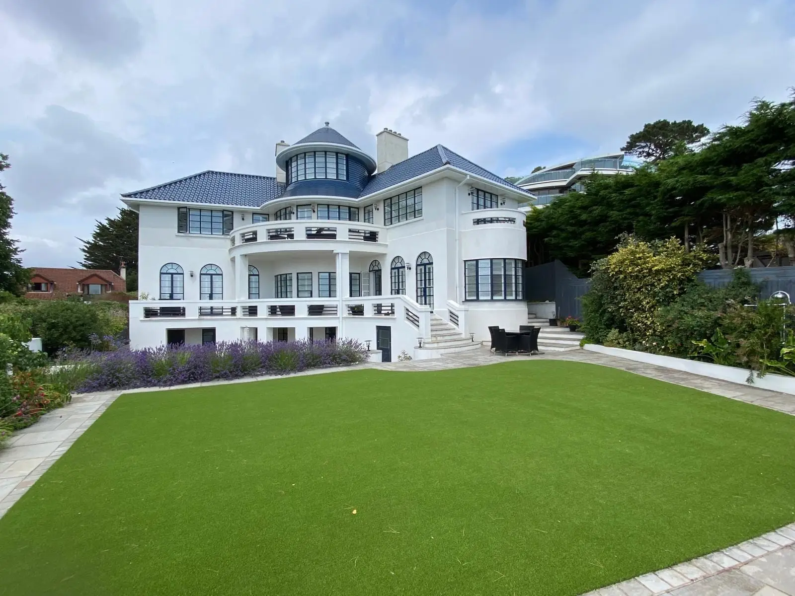 A restored 1930s Art Deco house with a blue glazed pantile roof and a turret, seen across the lawn