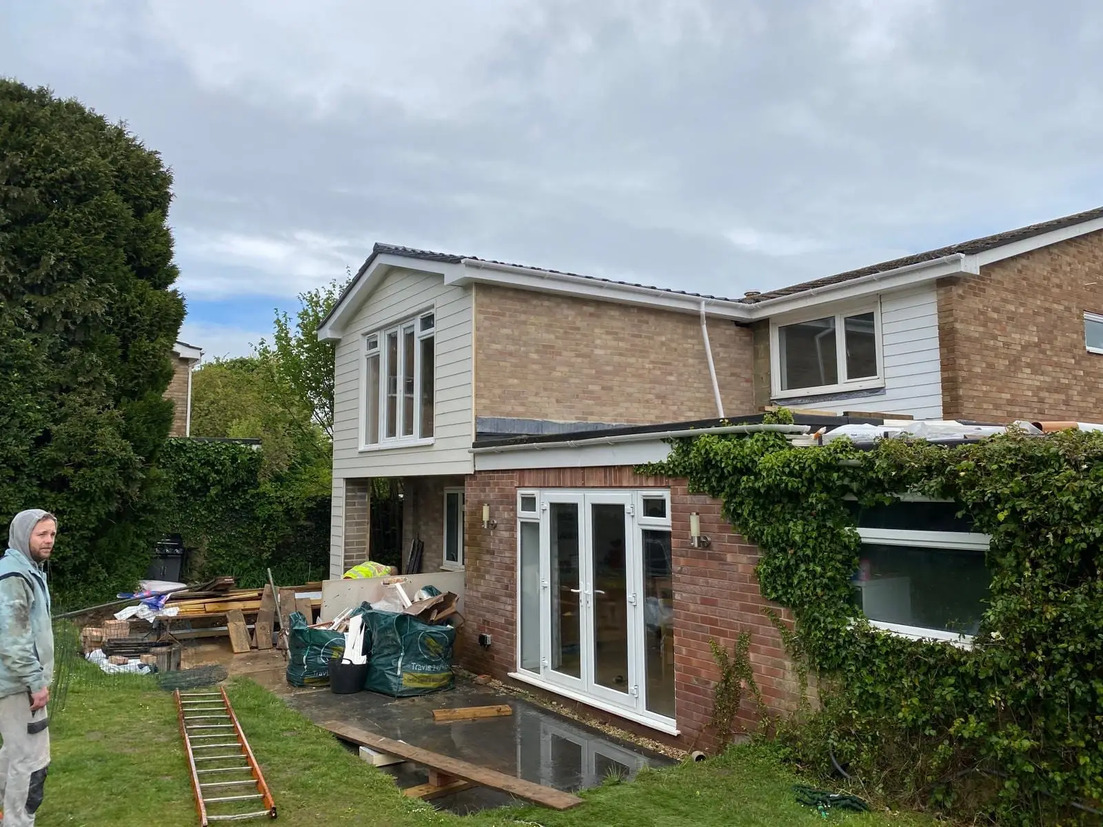 The new first floor built and clad, with ivy still covering the ground floor wall and materials stacked on the lawn