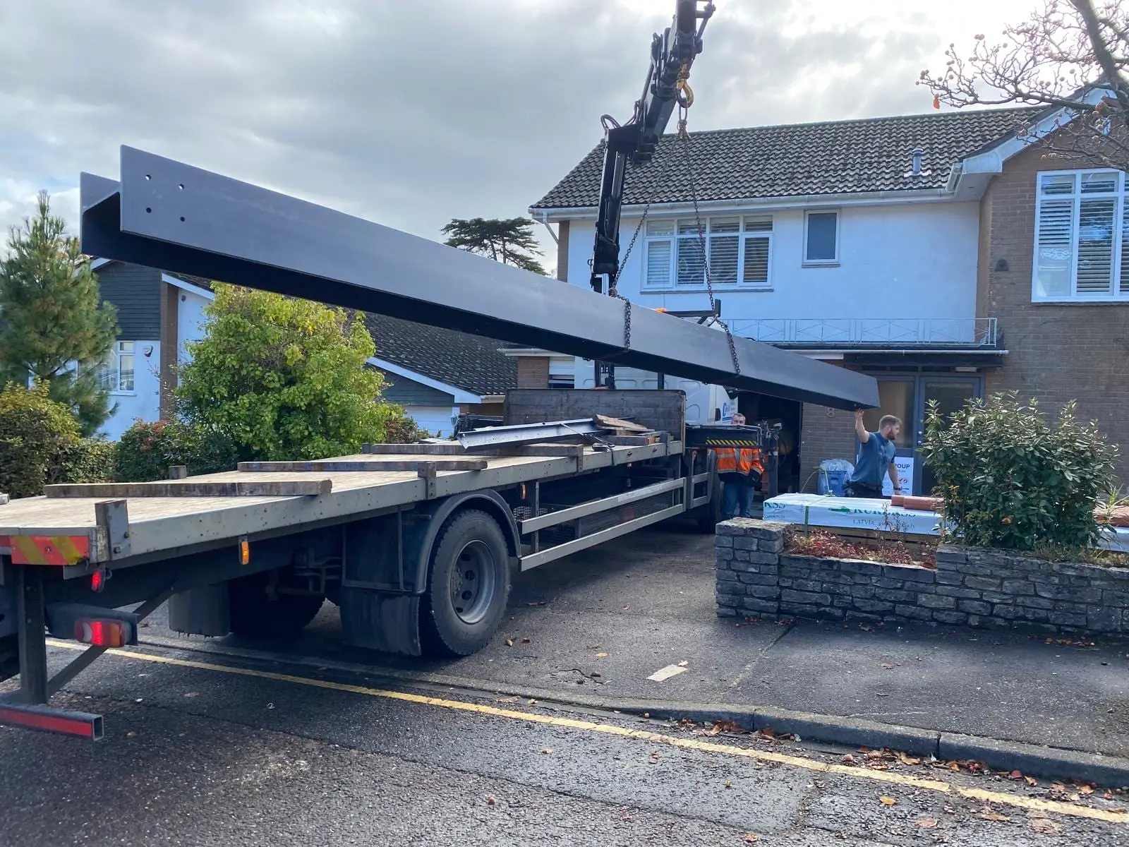 A steel beam lifted off the delivery lorry by the lorry's own crane, over the front garden