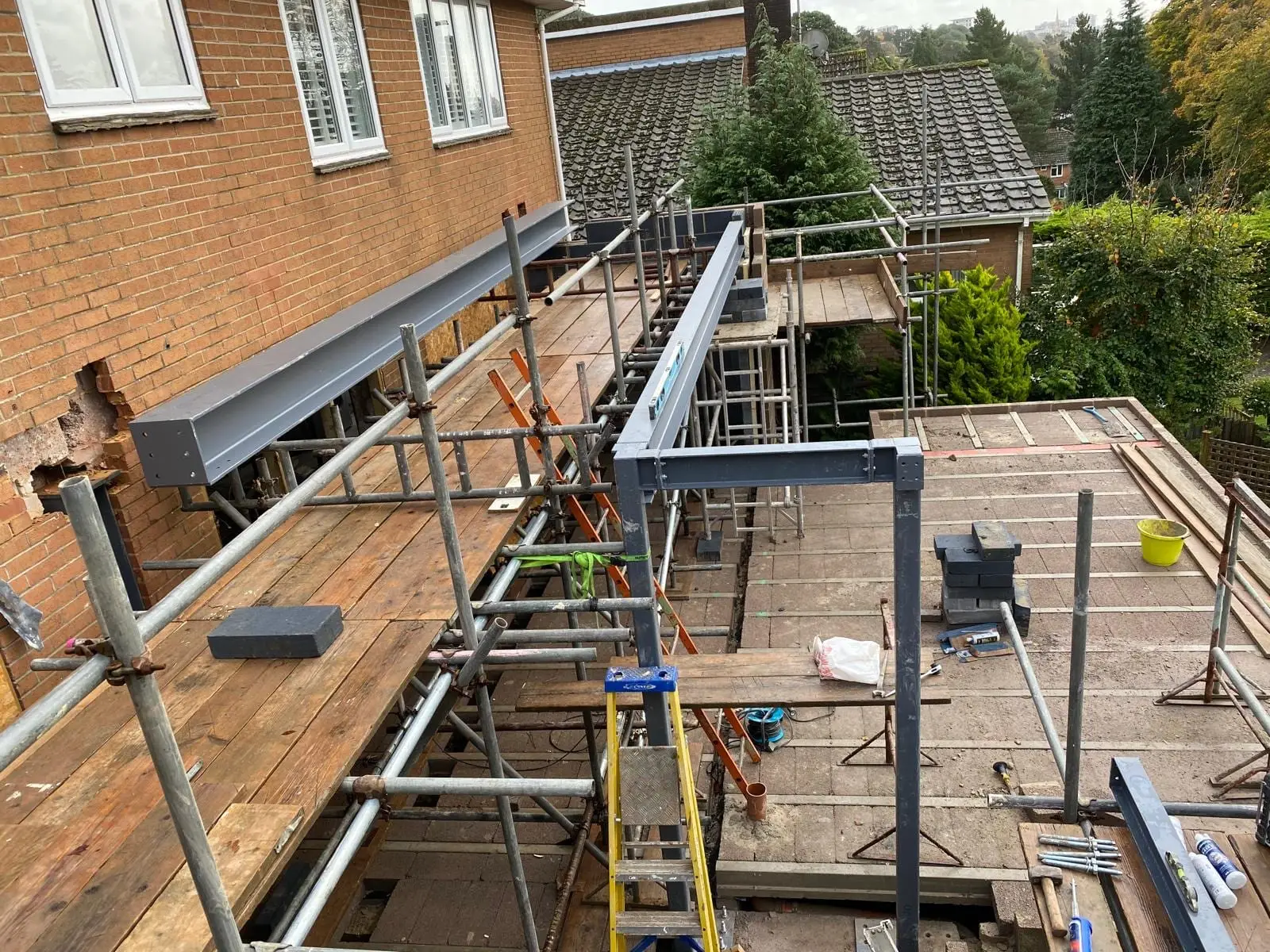 The steel goalpost frame bolted up on the terrace, with the beam back to the house behind it