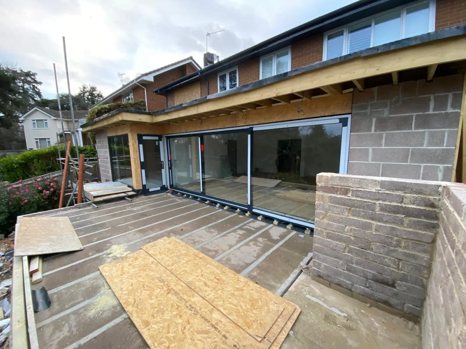 The extension in bare blockwork with the timber roof structure still exposed, seen across the terrace