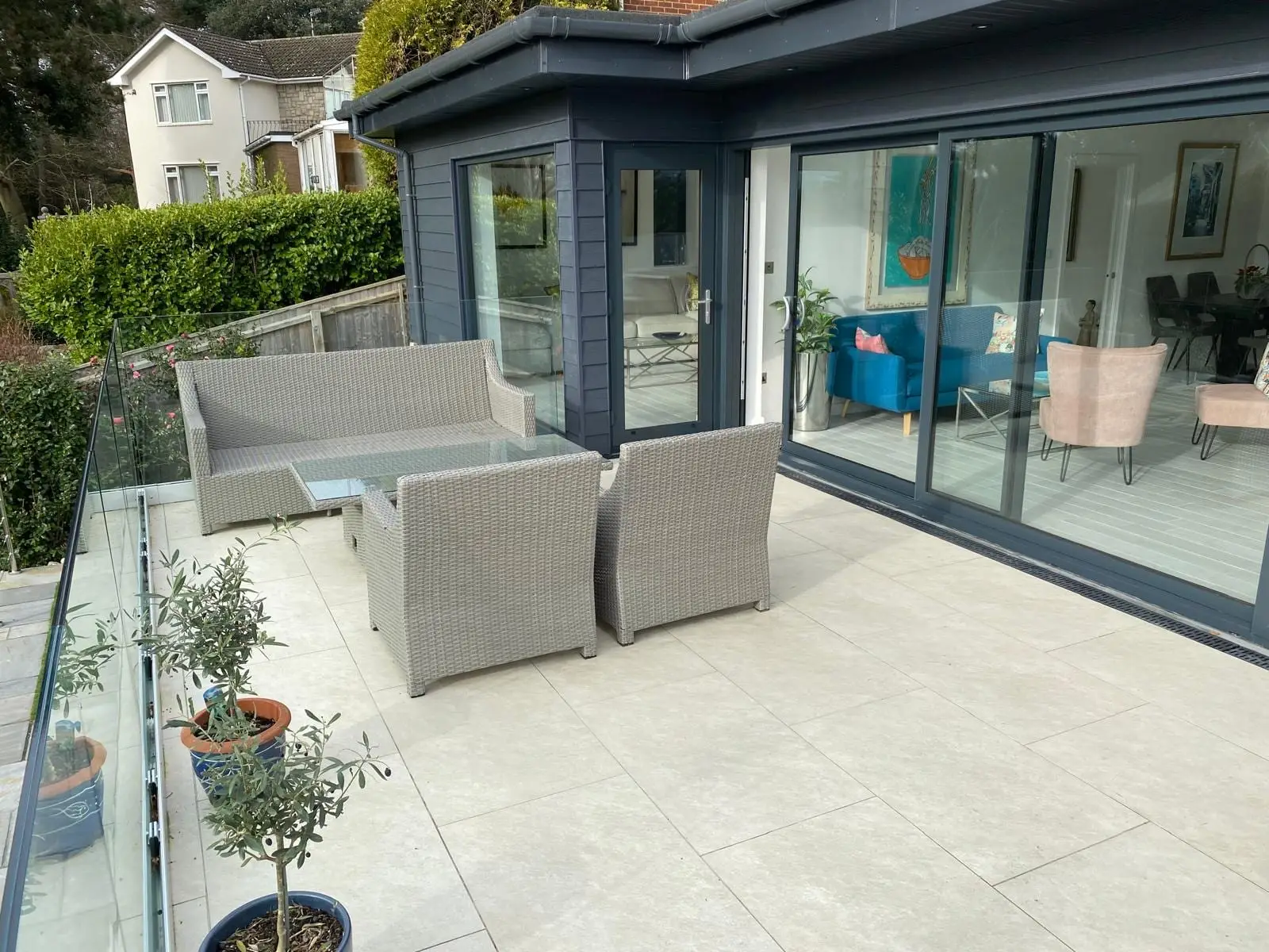 The finished terrace: porcelain paving, a frameless glass balustrade and the corner sliding doors into the new room